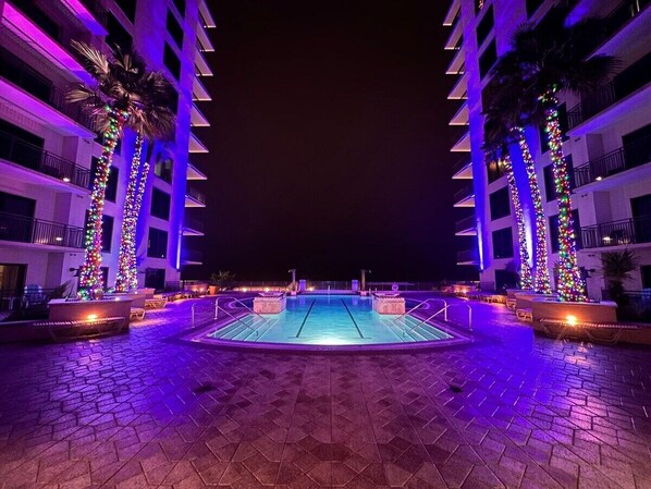 A swimming pool with a tiled deck, surrounded by palm trees and buildings with balconies.