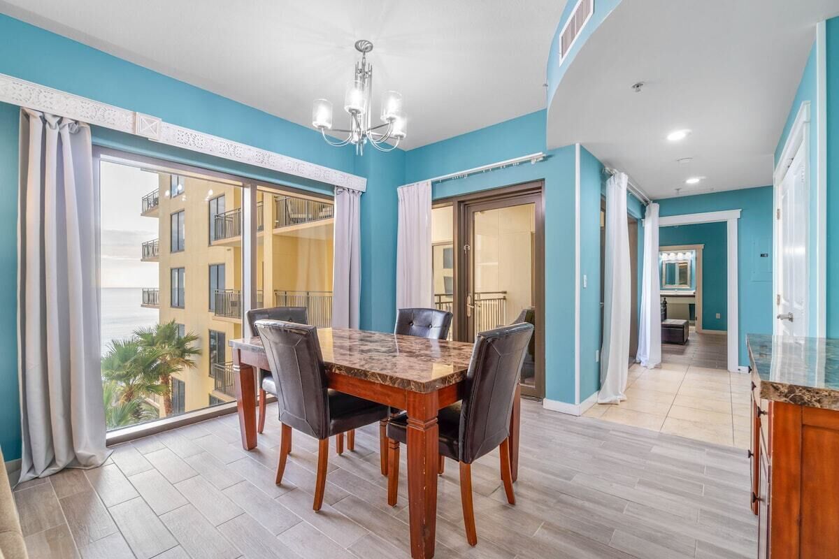 Un espace repas avec une table et des chaises en marbre, un lustre et une vue sur un immeuble doté de balcons.