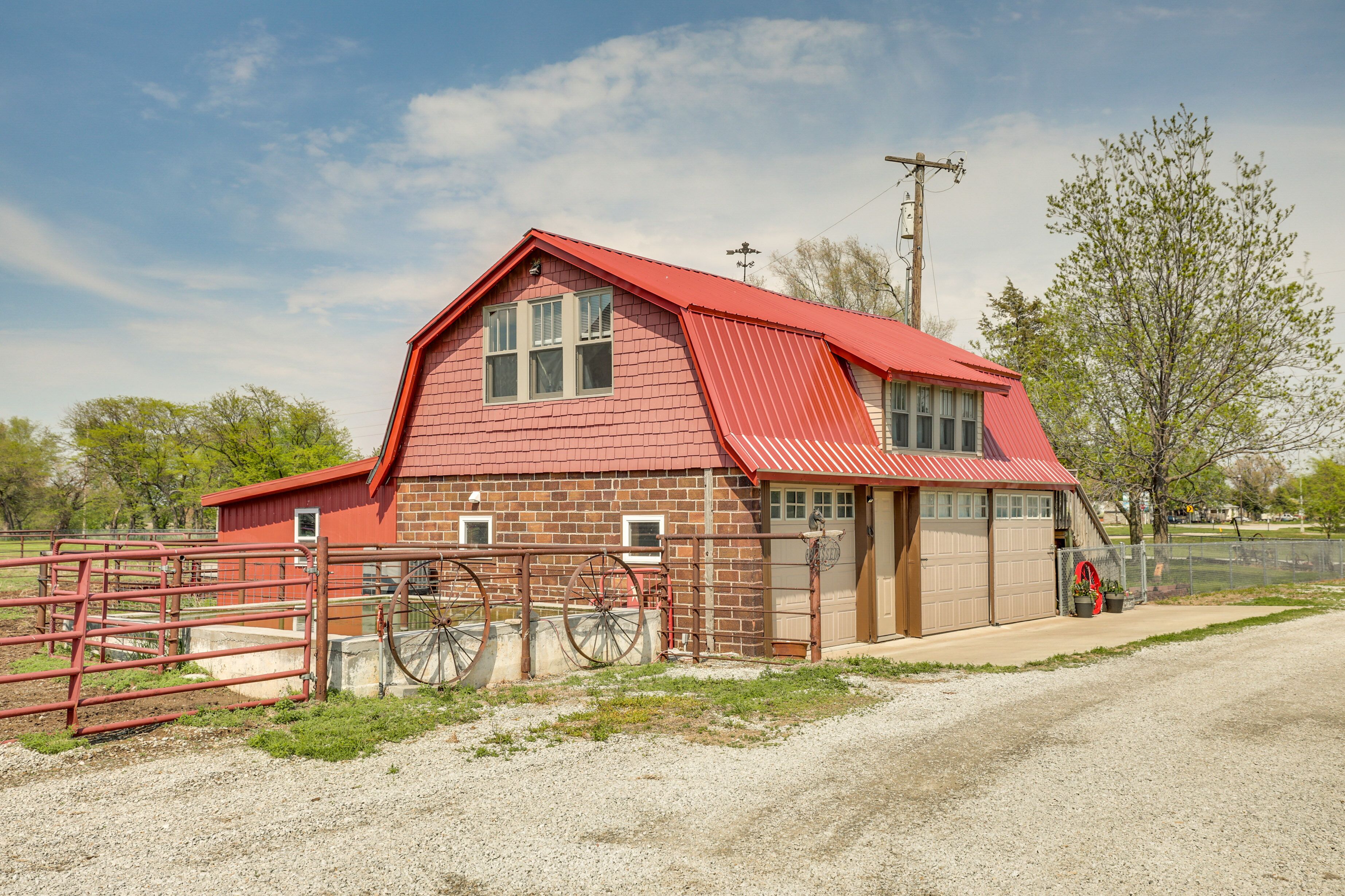 A red barn with a sloped roof, a fenced area with a gate, and a gravel driveway.
