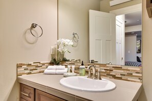 A bathroom with a white sink, a mirror, and a towel rack. There is a bottle of soap and a vase with flowers on the counter. - Walkable Portland Studio < 1 Mi to Dtwn! (Portland)