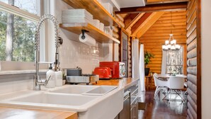 Una cocina moderna con un lavamanos blanco, grifo de acero inoxidable y una tostadora roja. Se aprecia un techo de madera y, al fondo, se ve el área de comedor.
