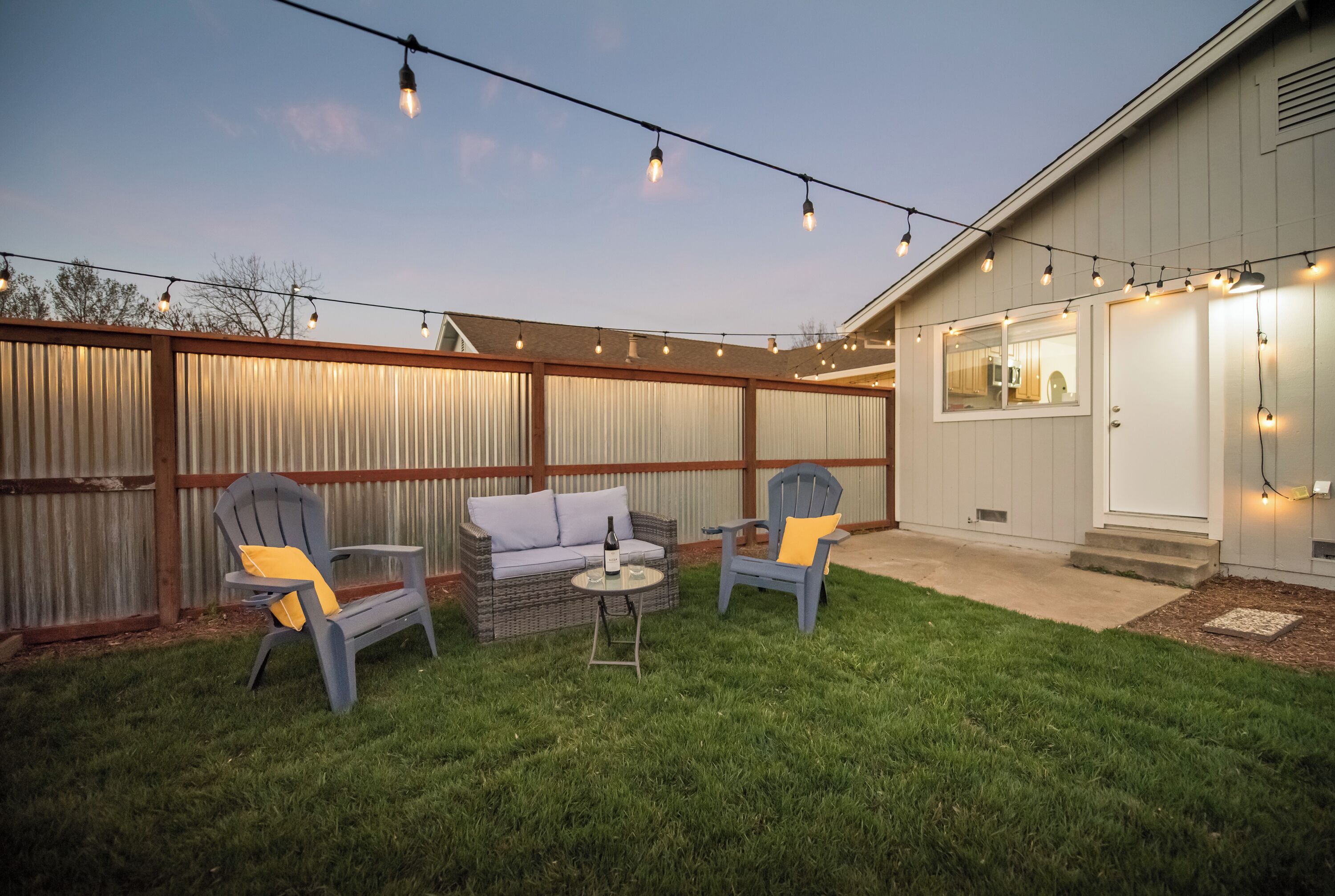 An outdoor patio with two chairs, a small table, and string lights.