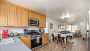 A kitchen with wooden cabinets, a microwave, stove, and sink. There is a dining area with a table and chairs. - 2 BD/1 BA Home- Wine Country Getaway (Santa Rosa)