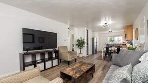 A modern living room with a TV, sofa, coffee table, and a dining area with chairs and a plant. - 2 BD/1 BA Home- Wine Country Getaway (Santa Rosa)