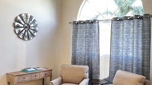 A room with two beige armchairs, a wooden side table with a blue object, and a wall clock. - Heated Pool Home with Southern Exposure! A Tropical Paradise! (Cape Coral)