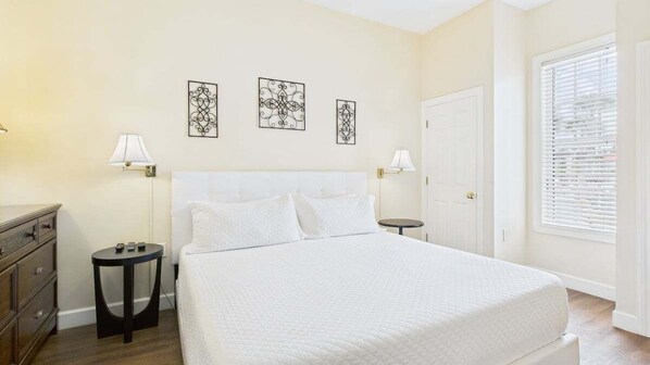 A bedroom with a large bed, two bedside tables, a dresser, and three wall-mounted artworks.