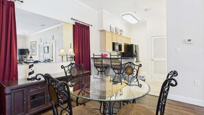 A dining area with a glass table and metal chairs, a kitchen with wooden cabinets, and a red curtain.