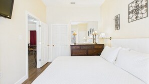 A bedroom with a large bed, a dresser, a mirror, and a television on the wall.