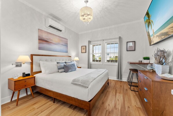 A bedroom with a wooden bed, bedside lamps, a large window, and a beach-themed painting.