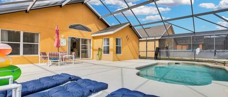 A covered outdoor swimming pool area with lounge chairs and a hot tub.