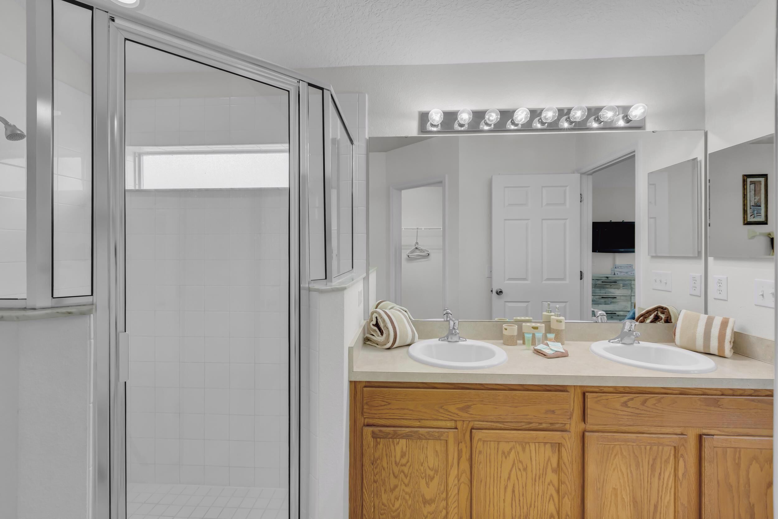 A modern bathroom with a glass shower enclosure, a double sink vanity, and a large mirror with built-in lighting.