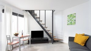 A modern living room with a staircase, a dining area with a TV, and a sofa with a yellow pillow. - Home2Book Disco Duplex in Las Américas Beach (Arona)