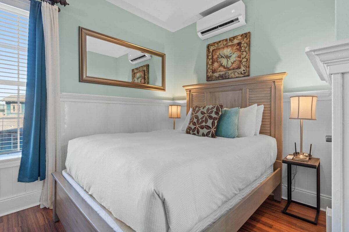 A neatly made bed with a headboard, a bedside lamp, and a wall-mounted air conditioner.