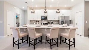 A modern kitchen with white cabinets, a central island with bar stools, and pendant lighting. - Stunning 4 Bed Private Villa close to Disney (Davenport)