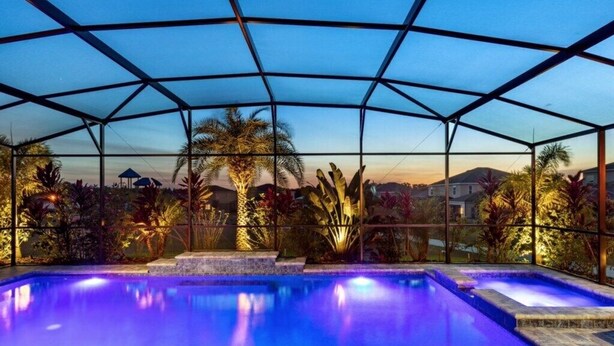 An indoor swimming pool with a glass ceiling, surrounded by tropical plants and a view of a cityscape. - Stunning 4 Bed Private Villa close to Disney (Davenport)