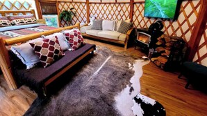 L’intérieur d’une yourte, avec un canapé, un téléviseur à écran plat, une cheminée et un plancher en bois.