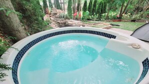 Un bain à remous bordé de carreaux bleus, entouré d’une végétation luxuriante et agrémenté d’une cascade en pierre.