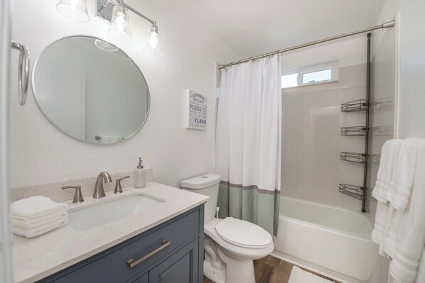 A modern bathroom with a round mirror, a sink, a toilet, and a shower area.