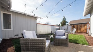 A backyard with wicker furniture, a small table with a bottle, and string lights.