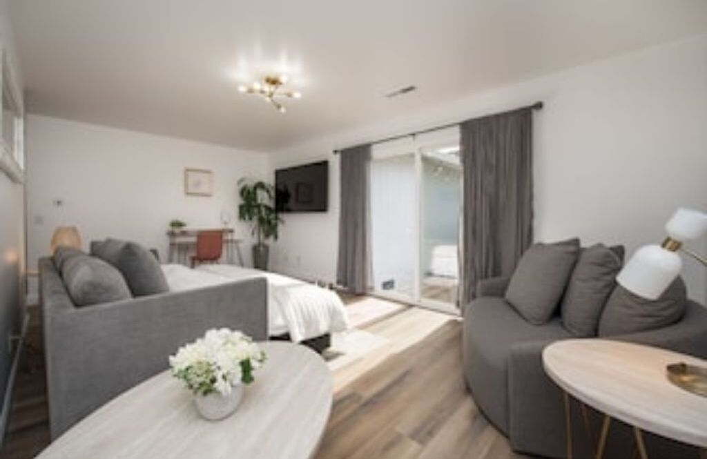 A modern hotel room with a bed, a sofa, a small table with a vase, and a TV on the wall.