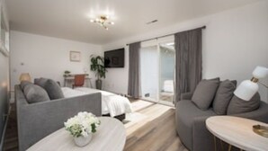 A modern hotel room with a bed, a sofa, a small table with a vase, and a TV on the wall.