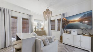 Un salon moderne doté d’un grand téléviseur à écran plat, d’un lustre et d’un parquet à motifs en chevrons.