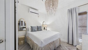 Un dormitorio con cama, lámpara de noche, espejo y ventana con cortinas.