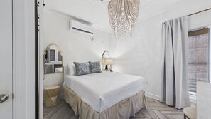 Un dormitorio con cama, lámpara de noche, espejo y ventana con cortinas.