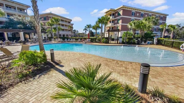 A swimming pool with lounge chairs and palm trees, surrounded by buildings with balconies.