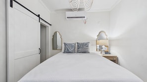 Une chambre à coucher comprenant un lit, une table de chevet, une lampe, un appareil de climatisation et une porte avec une poignée.