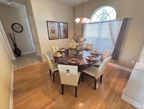 A dining area with a round table, six chairs, and a vase with flowers.