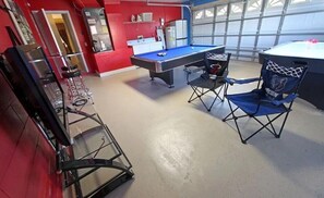 A pool table with chairs, a refrigerator, and a window in a room with red walls.