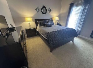A bedroom with a bed, two bedside lamps, a dresser, a desk, and a mirror on the wall.