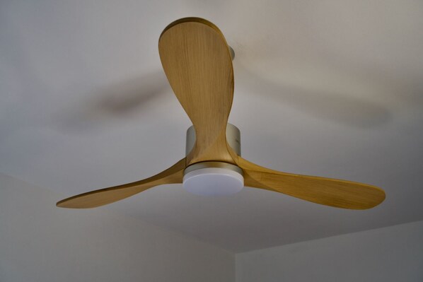 Un ventilateur de plafond doté de trois pales en bois et d’un moyeu central blanc.