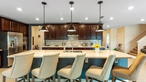 Una cocina moderna con armarios de madera oscura, una isla central con taburetes altos y lámparas colgantes.