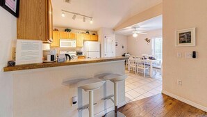 Een moderne keuken met houten kastjes, een bar met krukken, en een eethoek met witte stoelen.