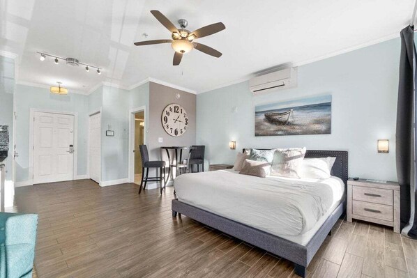 Un dormitorio moderno con una cama grande, un ventilador de techo, un reloj y un cuadro en la pared.