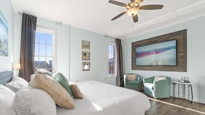 Habitación de hotel con una cama grande, ventilador de techo, televisor montado en la pared y vista a la ciudad por la ventana.
