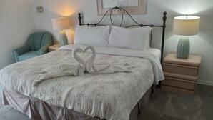 A neatly made bed with a floral bedspread and two swan-shaped pillows, a teal armchair, two bedside lamps, and a small bedside table with a lamp. - Fabulous 4 Bed South Facing Lake View Near Disney (Kissimmee)