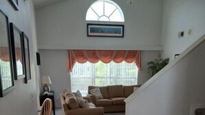 A spacious living area with a staircase leading to a second floor, a large window with curtains, and a framed picture on the wall. - Fabulous 4 Bed South Facing Lake View Near Disney (Kissimmee)