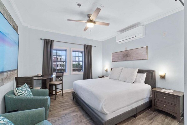 Ein Schlafzimmer mit Bett, Schreibtisch, Stuhl, Deckenventilator und einem Fenster mit Vorhängen.