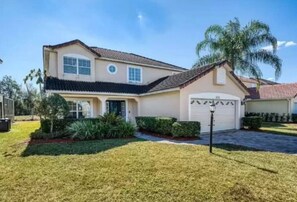 A two-story house with a garage, a well-maintained lawn, and a palm tree.