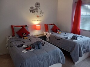 A bedroom with two beds, each with Mickey Mouse-themed bedding, a wall decoration, and a red curtain.