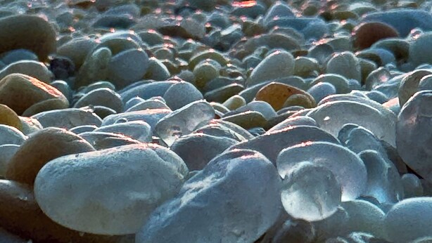Un atardecer sobre una playa de guijarros con el sol reflejándose en el agua.