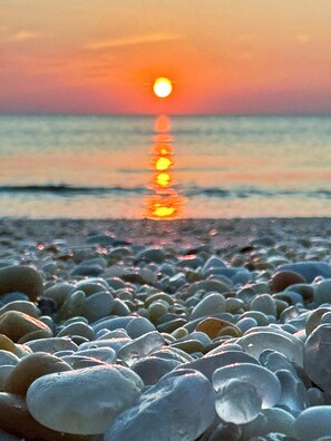 A sunset over a pebble beach with the sun reflecting on the water. - Maggie May Beach Cottage @ Cape May, NJ (Lower Township)