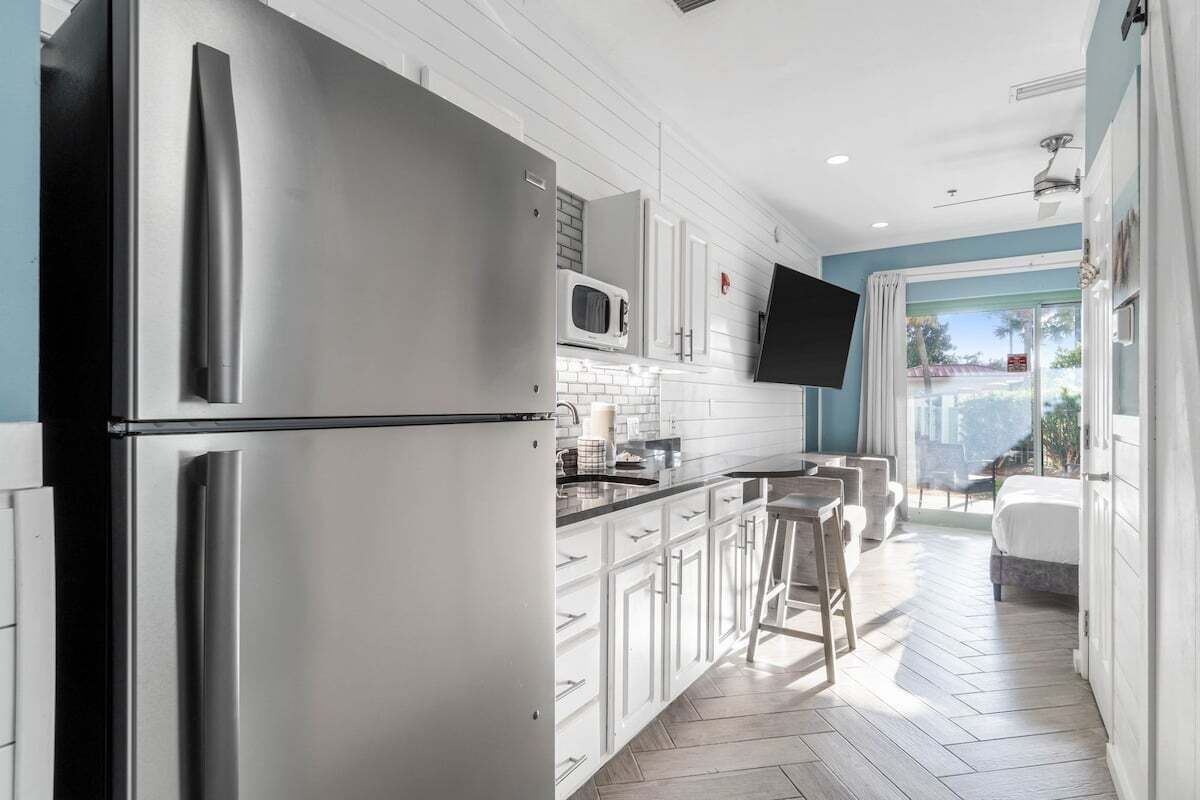 A modern kitchen with stainless steel appliances, white cabinetry, and a large window overlooking a balcony.