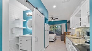 A modern kitchen with white cabinetry, a large island with a sink, and a view of the outdoors. - Beach Happy 100-steps to beach-Sleeps 2 (Seacrest)