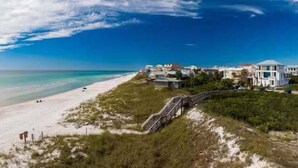 A beach with a white sandy shore, a clear blue sky, and a few buildings with a bridge leading to them. - Beach Happy 100-steps to beach-Sleeps 2 (Seacrest)