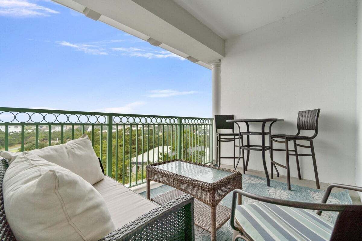 Een balkon met rieten meubilair, een glazen tafel en uitzicht op groen.