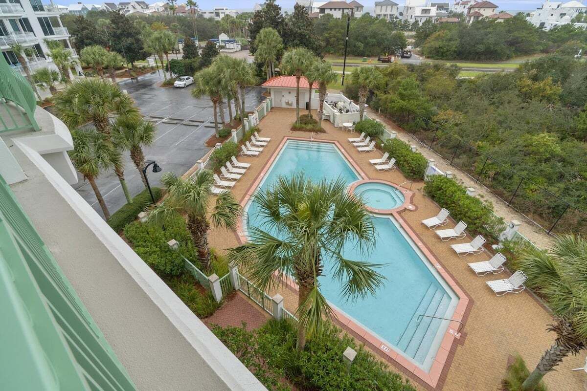 A pool area with lounge chairs, palm trees, and a view of the surrounding neighborhood.
